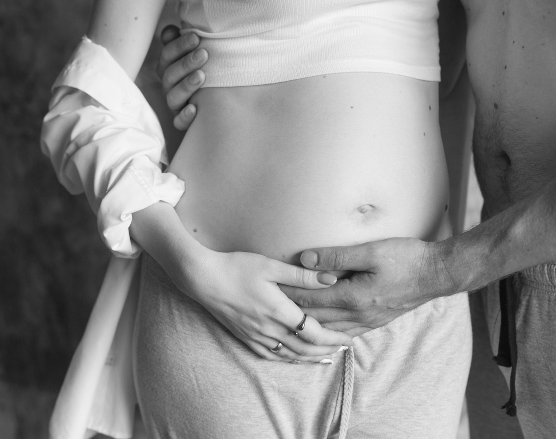 Schwarz Weiss Bild einer Frau und eines Mannes. Beide halten die Hände schützend vor dem Bauch, Der Mnn ist Oberkörperfrei, die Frau leicht bekleidet, sie hatte einen Kaiserschnitt.